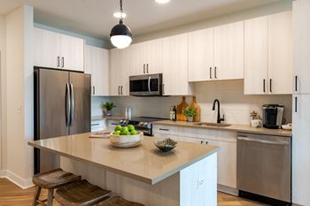 A kitchen with white cabinets and a large island with a bowl of fruit on it